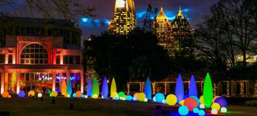 Colorful illuminated sculptures in a park with a city skyline at night, featuring vibrant lights and festive decorations.