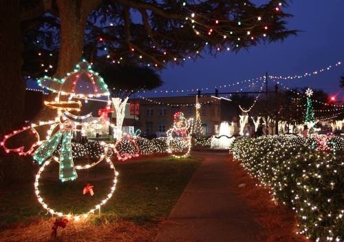 Colorful holiday lights decorate a pathway with snowman figures and festive decorations in a nighttime setting.