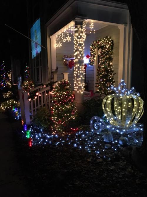 A festive porch decorated with colorful lights, a Christmas tree, and a glowing crown-shaped ornament.