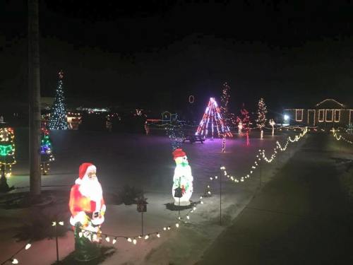 Colorful Christmas lights and decorations illuminate a festive outdoor scene with Santa and snowman figures.