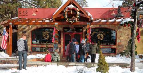 A snowy scene outside a festive restaurant, with people gathered and holiday decorations adorning the entrance.