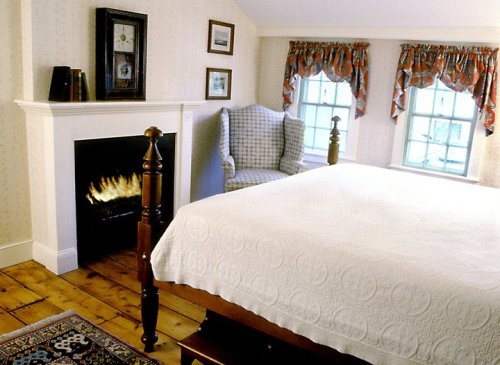Cozy bedroom with a bed, armchair, fireplace, and decorative curtains. Warm, inviting atmosphere.