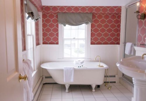 A bright bathroom featuring a vintage clawfoot tub, elegant wallpaper, and a stylish sink with natural light.