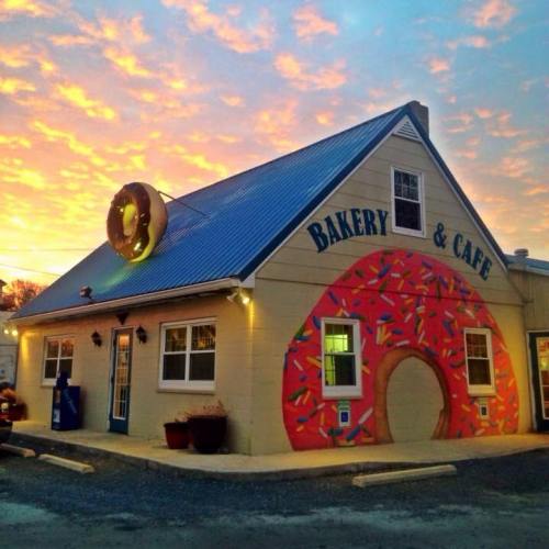 A bakery and café building with a colorful donut mural, set against a vibrant sunset sky.