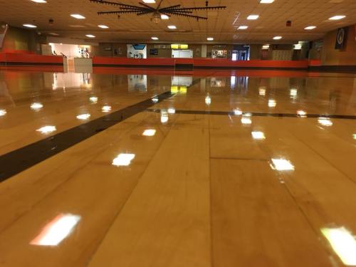 A polished wooden gym floor reflecting overhead lights, with a blurred background of a recreational space.
