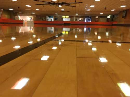 A polished wooden gym floor reflecting overhead lights, with a blurred background of a recreational space.