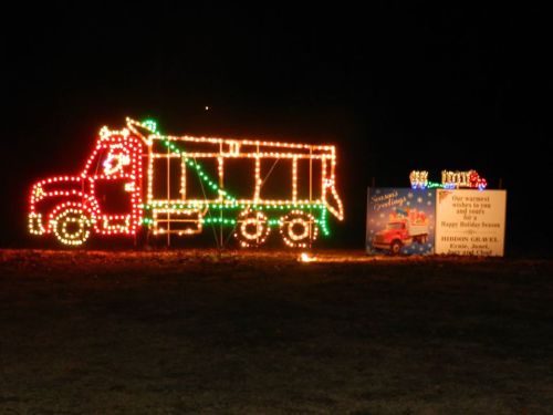 A brightly lit truck made of holiday lights next to a festive sign wishing a happy holiday season.