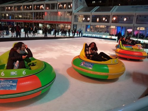 People enjoying bumper cars on an ice rink, surrounded by festive lights and a winter village atmosphere.