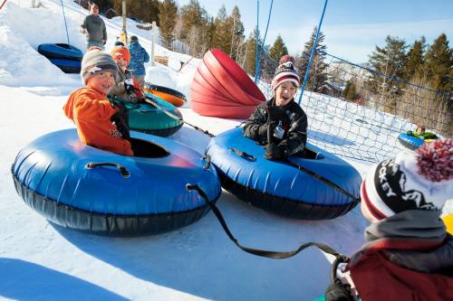 Children enjoying a snow tubing activity, smiling and sitting in colorful inflatable tubes on a snowy hill.