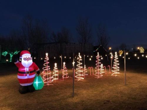A large inflatable Santa stands among illuminated Christmas trees and candy canes in a festive outdoor display at night.