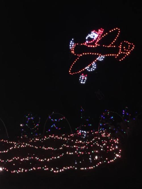 A colorful light display of an airplane flying above a garden of twinkling lights at night.