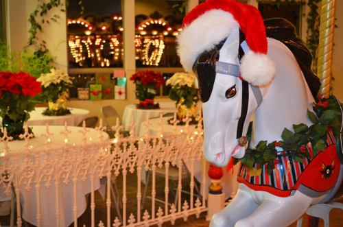 A festive carousel horse wearing a Santa hat, surrounded by holiday decorations and twinkling lights.