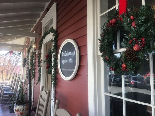 A festive porch with holiday wreaths and a sign for "The Dillsboro Square Hotel" on a red wooden building.
