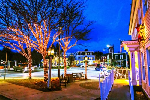 A charming town square at dusk, adorned with twinkling lights on trees and buildings, creating a festive atmosphere.
