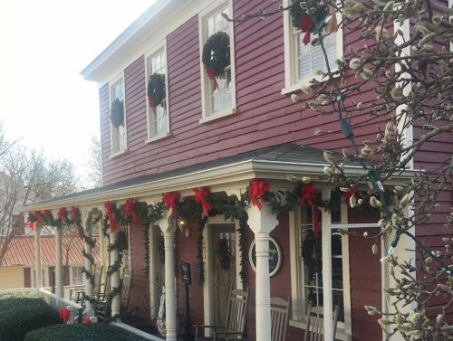 A festive house decorated with wreaths and red bows, featuring a porch with rocking chairs and holiday lights.