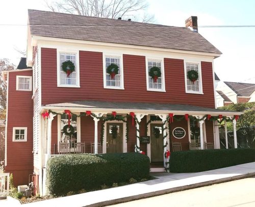 A charming red house decorated with wreaths and holiday garlands, featuring a welcoming porch and winter scenery.