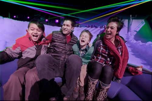 A joyful family of four enjoying a ride with colorful laser lights in a snowy setting, all smiling and laughing.