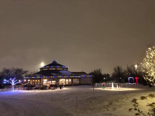 A snowy scene at night featuring a round building adorned with colorful lights and illuminated trees.