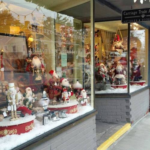 A festive window display featuring antique decorations, nutcrackers, and Santa figures, surrounded by faux snow.