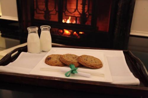 A tray with three cookies, a note tied with a green ribbon, and two bottles of milk in front of a cozy fireplace.