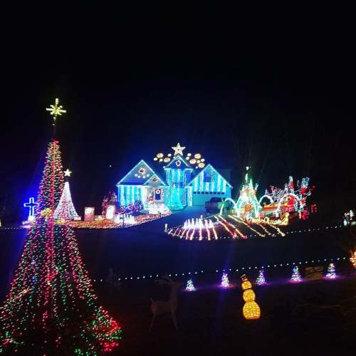 A brightly lit house decorated with colorful Christmas lights, surrounded by festive displays and a glowing tree.