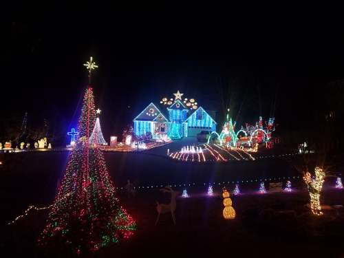 A festive house illuminated with colorful Christmas lights, featuring a decorated tree and various holiday displays.