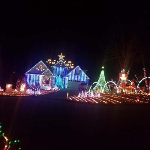 A brightly lit house decorated with colorful Christmas lights, featuring trees, stars, and festive displays in the yard.