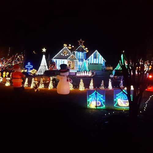 A festive display of colorful Christmas lights, decorations, and a snowman in a nighttime setting.