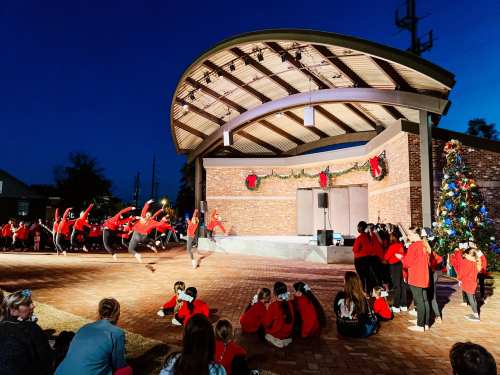 A dance performance on stage at night, with performers in red outfits and an audience seated nearby, decorated for the holidays.