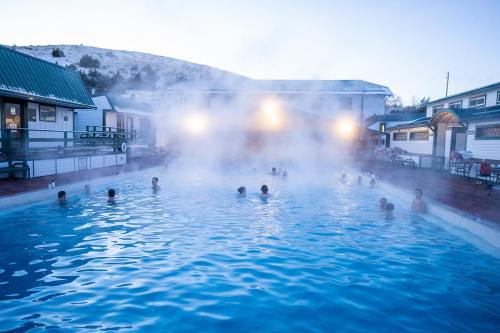 A steaming outdoor pool surrounded by buildings, with people enjoying the warm water under a misty sky.