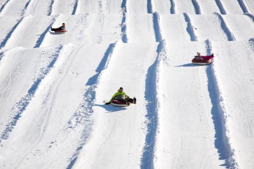 Three people sledding down snowy slopes on inflatable tubes, surrounded by white snow and ridged tracks.