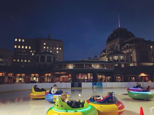 Colorful bumper cars on an ice rink at night, with a historic building illuminated in the background.