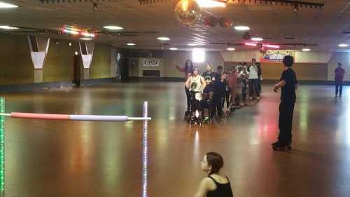 A roller skating rink with people skating and a disco ball overhead, colorful lights illuminating the space.