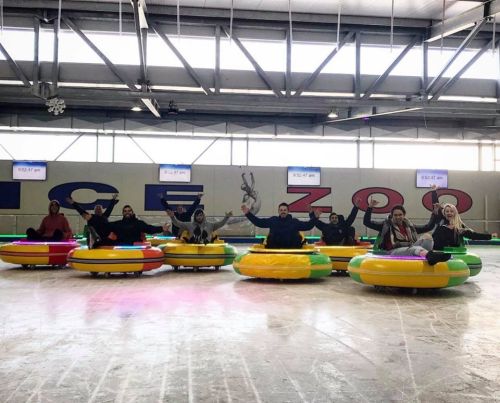 A group of people enjoying bumper cars on ice, smiling and posing in colorful inflatable rings at an ice rink.