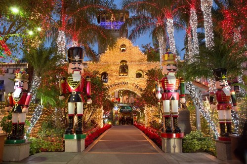 Colorful holiday display featuring large nutcracker figures and festive lights adorning a building and palm trees.