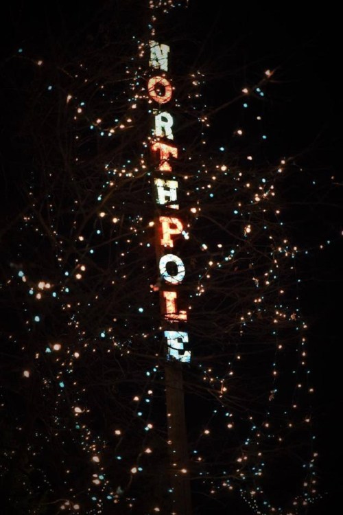A brightly lit sign reading "NORTH POLE" adorned with colorful lights against a dark night sky.