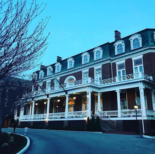 Historic building with a grand porch, surrounded by trees, illuminated at dusk. Flags adorn the front.