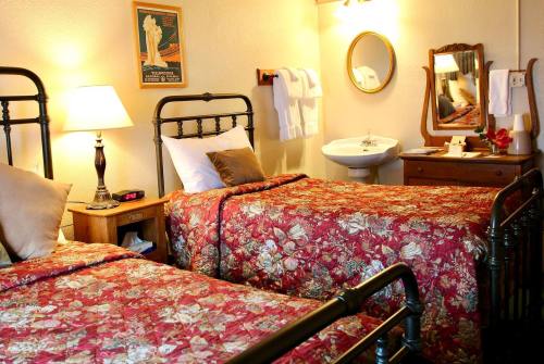 Cozy hotel room with two beds, floral bedding, a lamp, mirror, and a sink, creating a warm, inviting atmosphere.