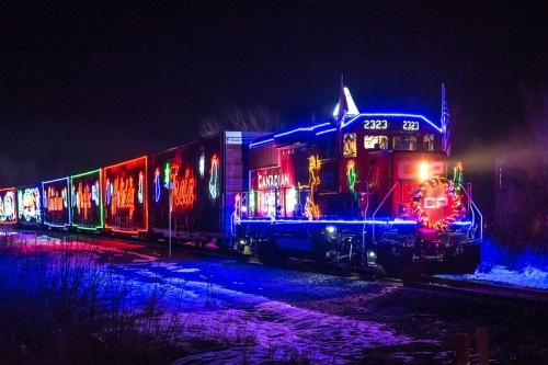 A brightly lit train decorated with colorful holiday lights travels through a snowy landscape at night.
