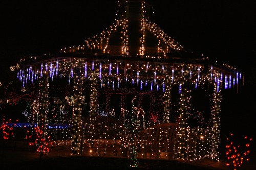 A beautifully lit gazebo adorned with colorful holiday lights and icicle decorations, set against a dark night sky.