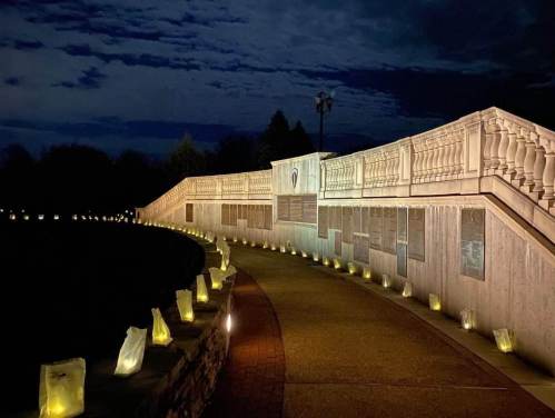 A softly lit pathway lined with luminaries, leading to a memorial wall under a night sky.