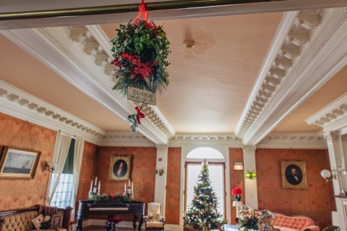 A festive room decorated for Christmas, featuring mistletoe, a tree, and vintage portraits on the walls.