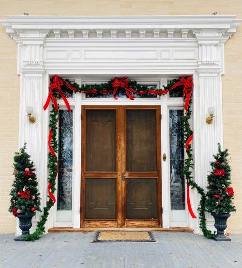 A festive entrance with a wooden door, adorned with red bows, greenery, and Christmas decorations on either side.