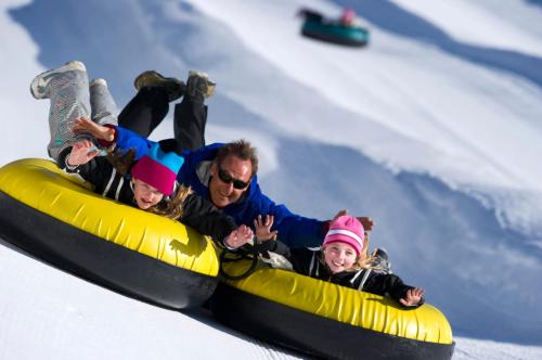 A man and two girls joyfully sledding down a snowy hill on yellow inflatable tubes.