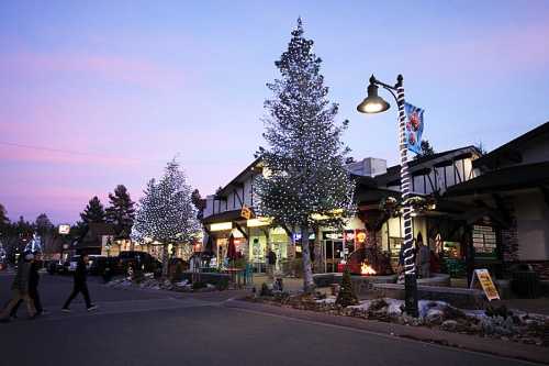 A charming street scene with festive lights on trees, shops, and a colorful sunset sky.