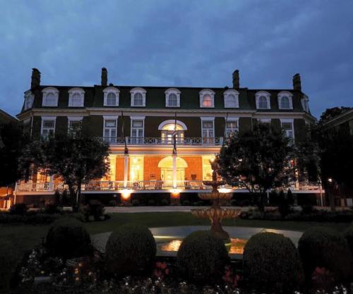 A grand historic mansion illuminated at dusk, featuring a fountain and landscaped gardens in the foreground.
