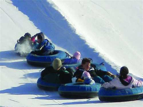 A group of people sliding down a snowy hill on inflatable tubes, enjoying a winter day.