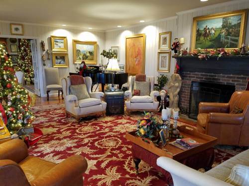 Cozy living room decorated for the holidays, featuring a Christmas tree, armchairs, and a piano by a fireplace.