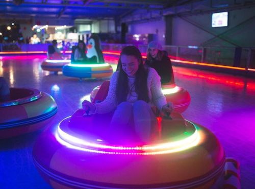 A girl enjoys riding a colorful bumper car with vibrant lights in an amusement venue.