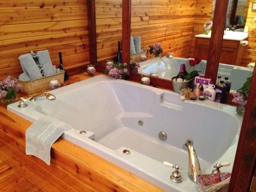 A cozy bathroom featuring a large white bathtub surrounded by wooden walls, flowers, and toiletries.